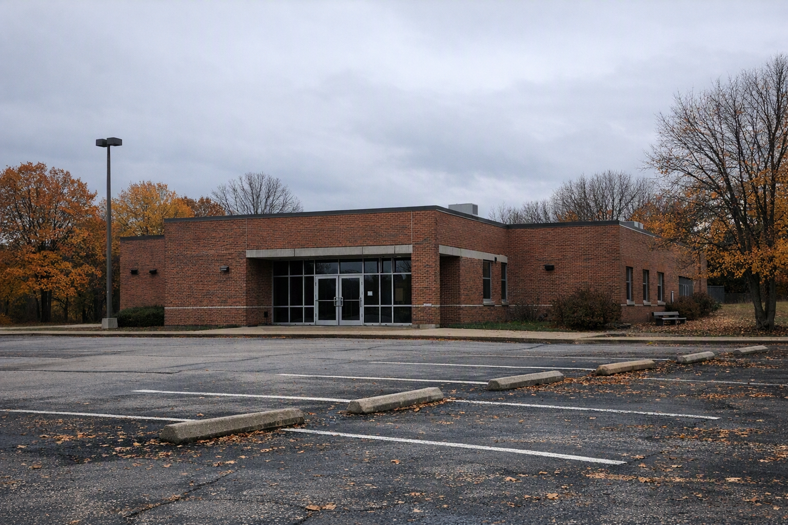 An empty brick college building with locked glass doors and a mostly vacant parking lot on an overcast day.